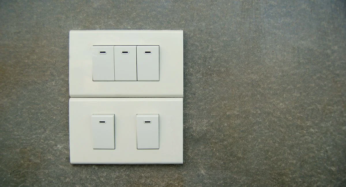 Minimalist photo of white electrical rocker switches on a textured stone wall background.