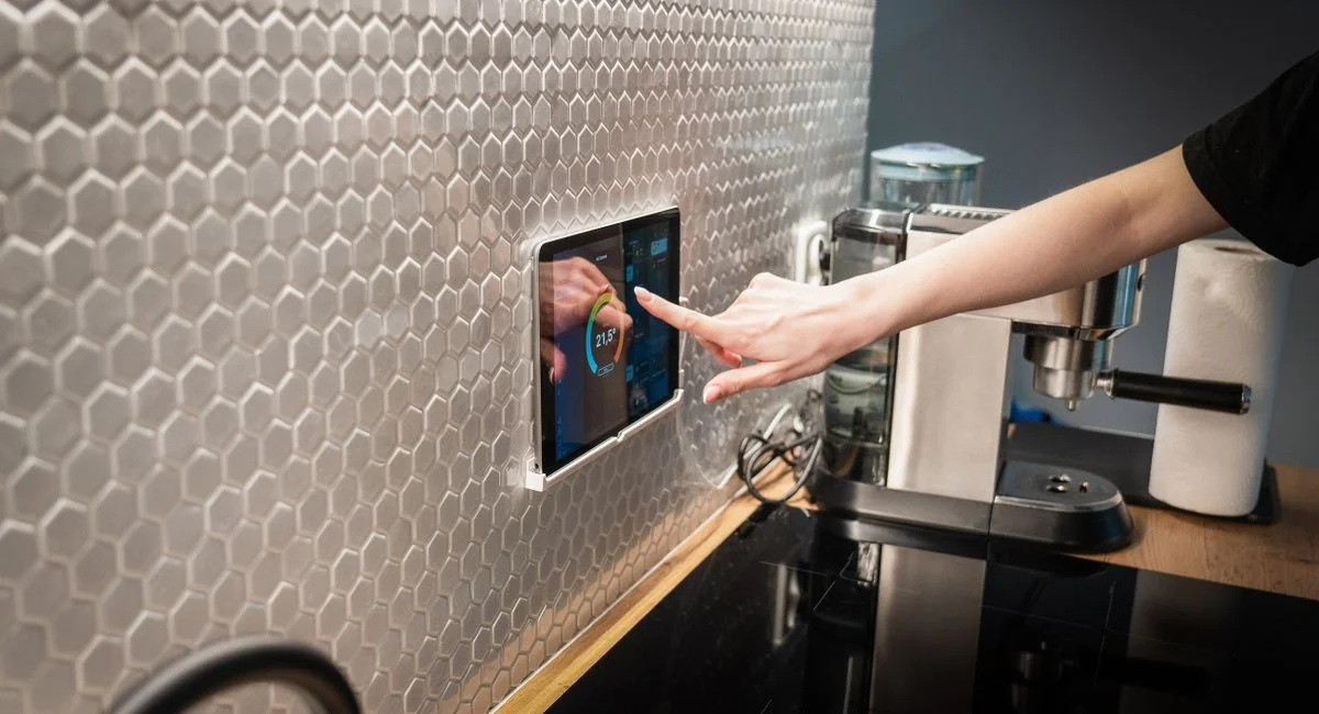 A modern kitchen with a touchscreen smart home control panel integrated into a hexagon-patterned wall.