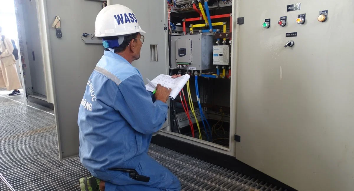 Engineer in uniform inspecting an electrical control panel in an industrial setting.