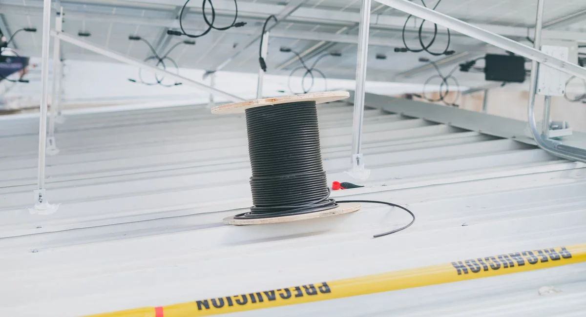 Coiled cable on a rooftop with solar panels, showcasing electrical installation for renewable energy.