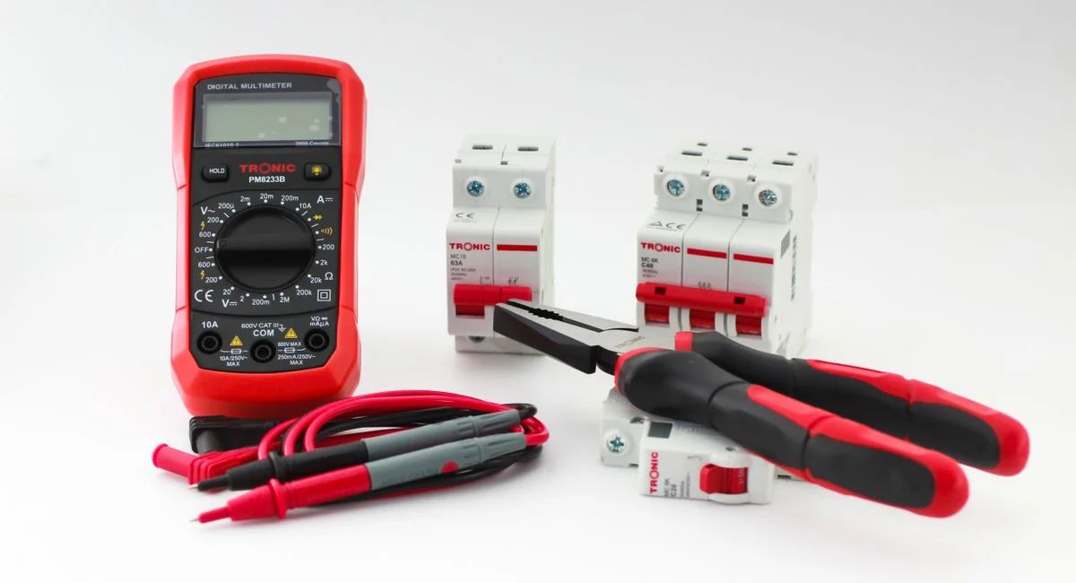 Close-up of a digital multimeter with electrical tools and circuit breakers on a white background.